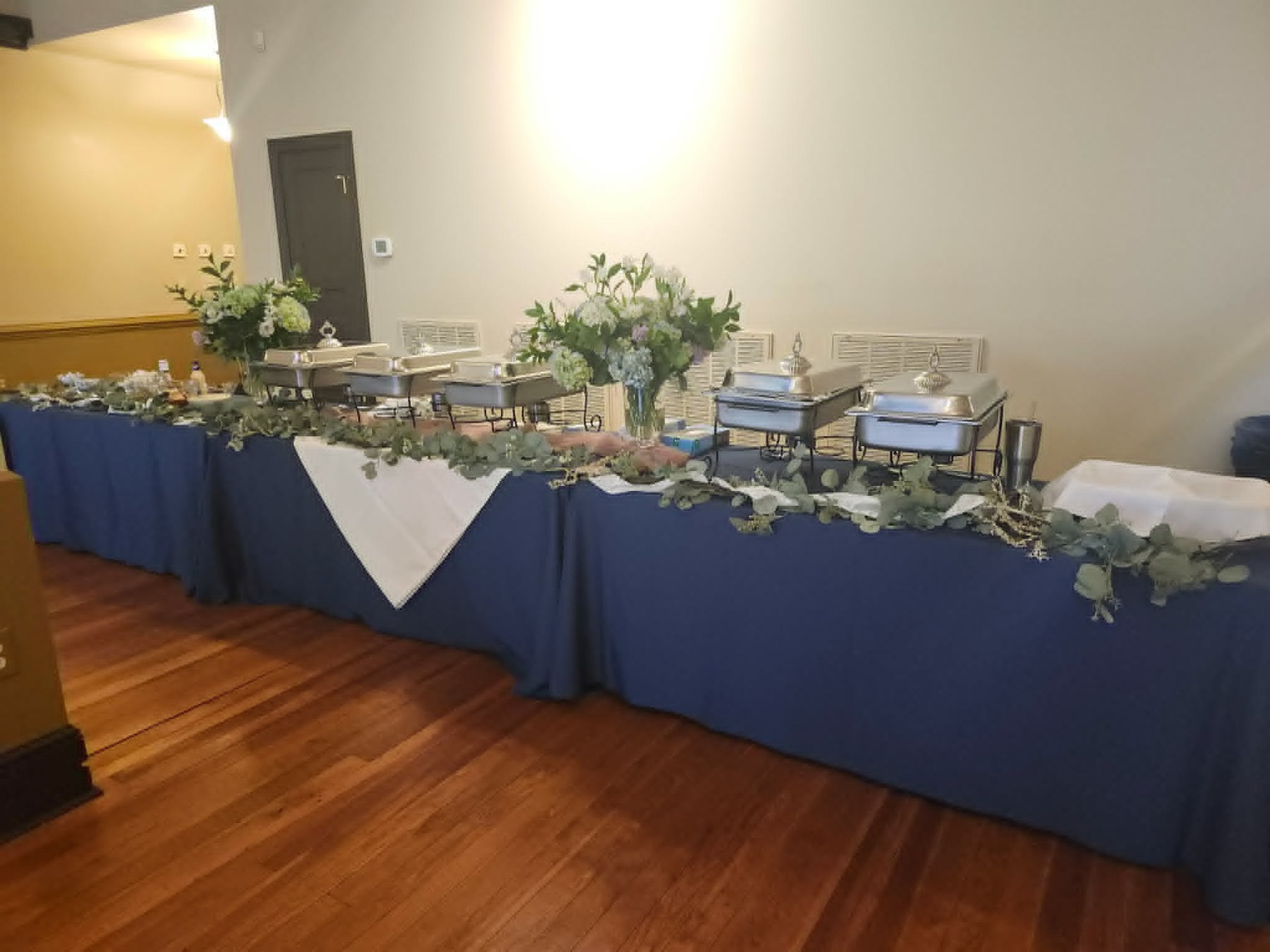 Long buffet table with chafing dishes, florals, and blue and white linens