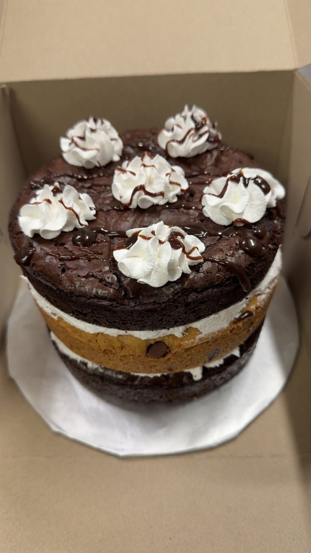 Layered chocolate brownie and cookie cake topped with whipped rosettes