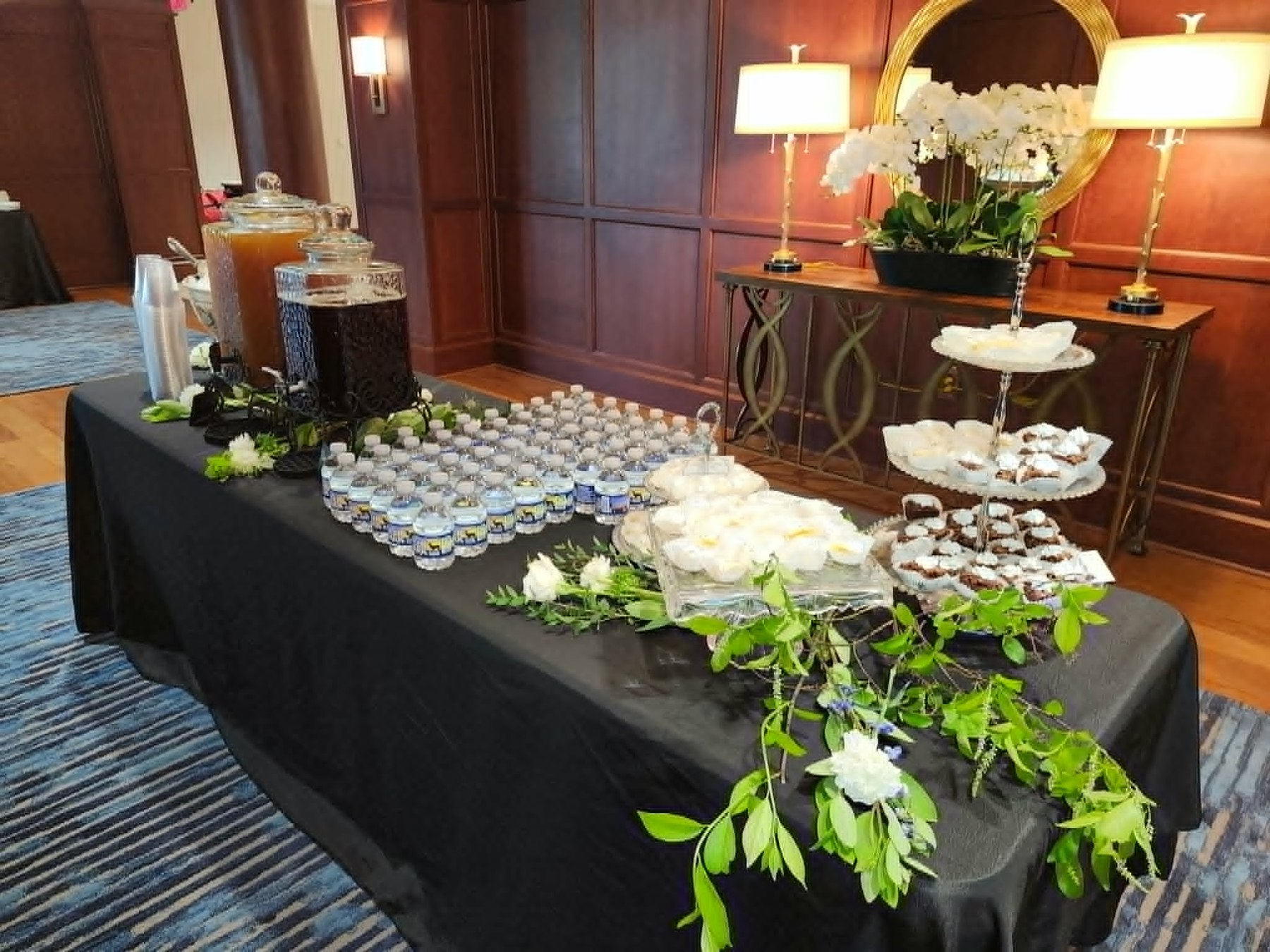 Professional event beverage and dessert station with greenery and tiered sweets