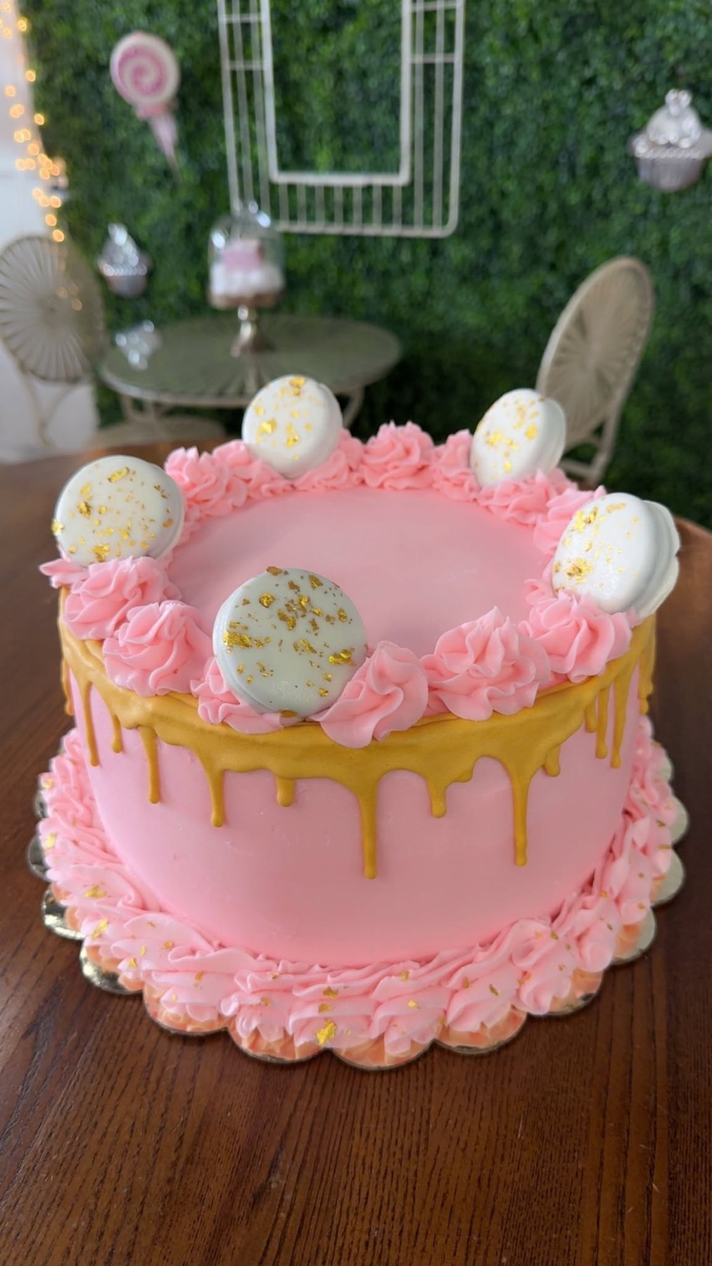 Pink celebration cake with gold drip, piped flowers, and white chocolate decorations