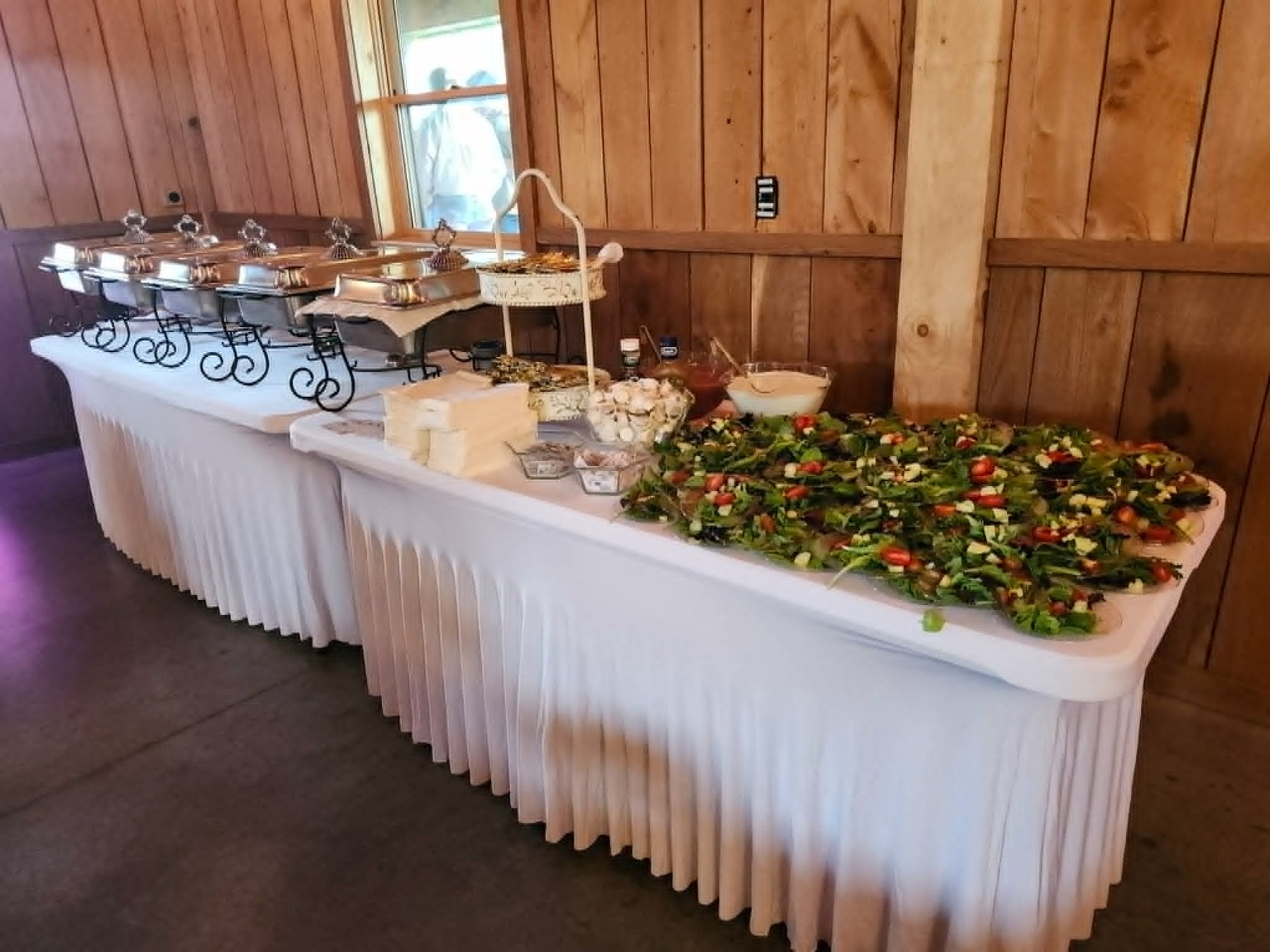Rustic buffet with chafing dishes, salad, sauces, and white linens