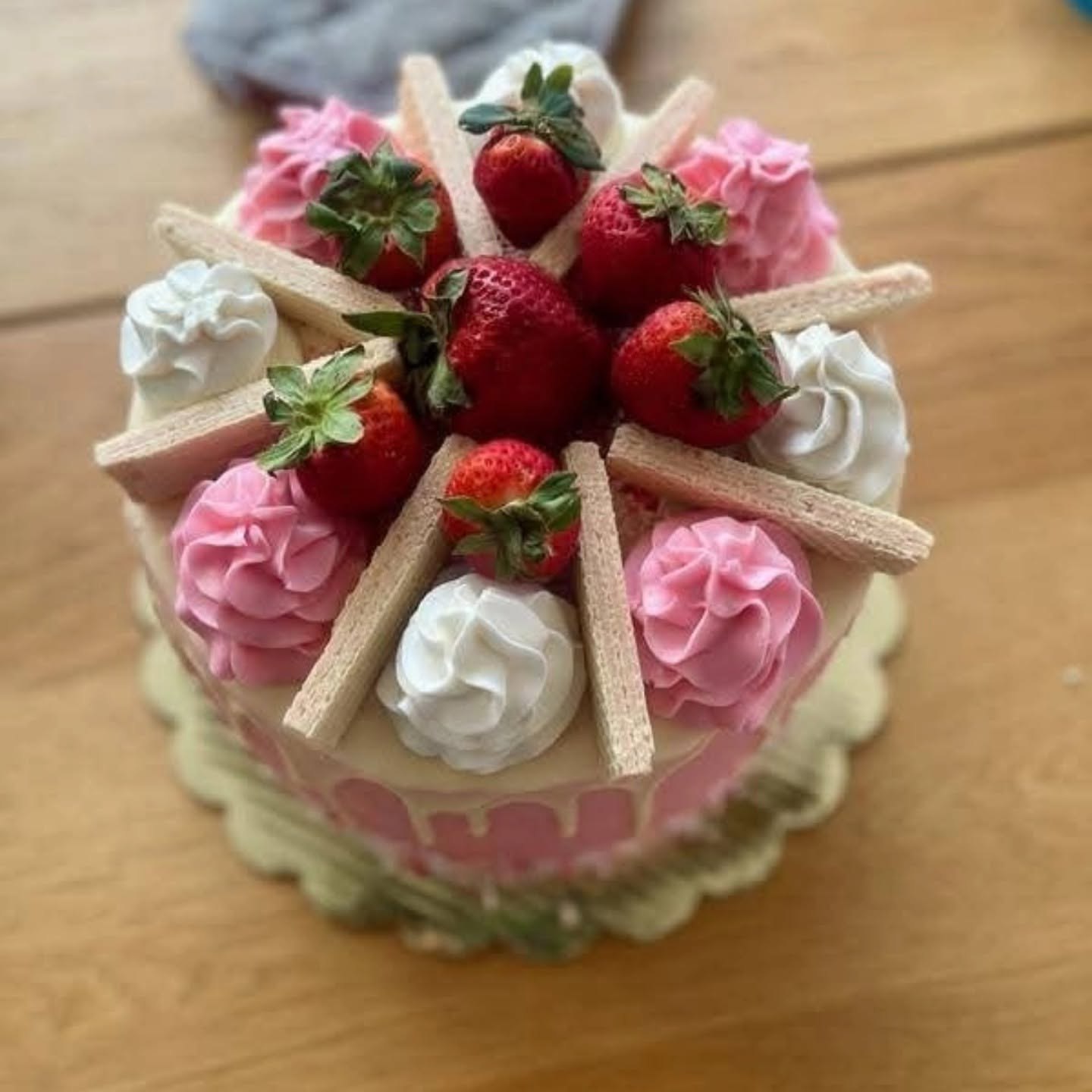 Strawberry celebration cake with pink and white piping, fresh strawberries, and wafer cookies