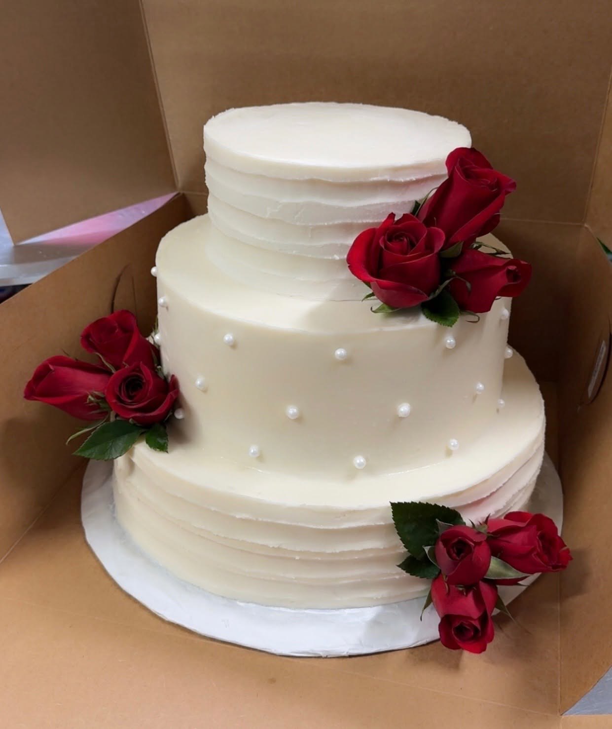 Three-tier white wedding cake accented with deep red roses