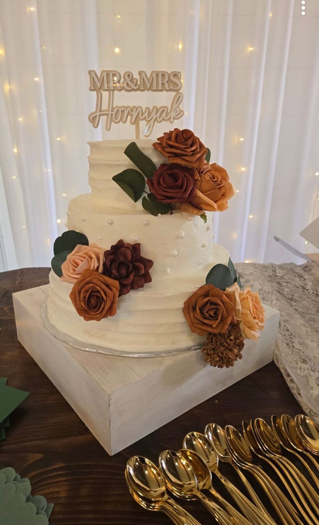 Three-tier white wedding cake with warm rust and burgundy floral accents