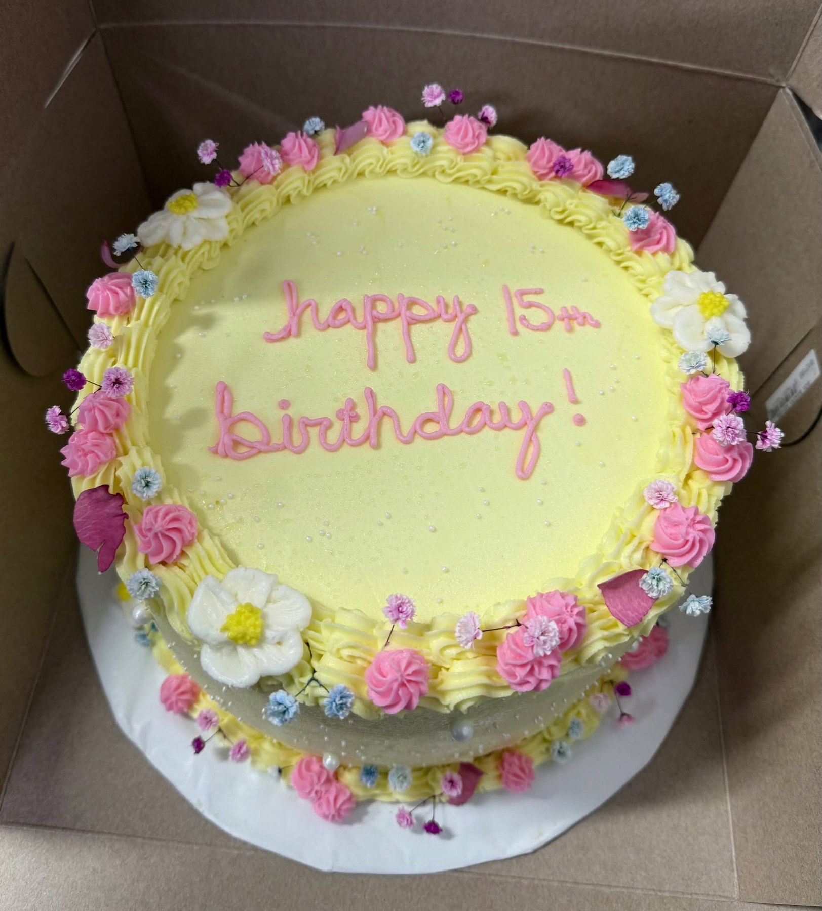 Yellow birthday cake decorated with pink and white flowers